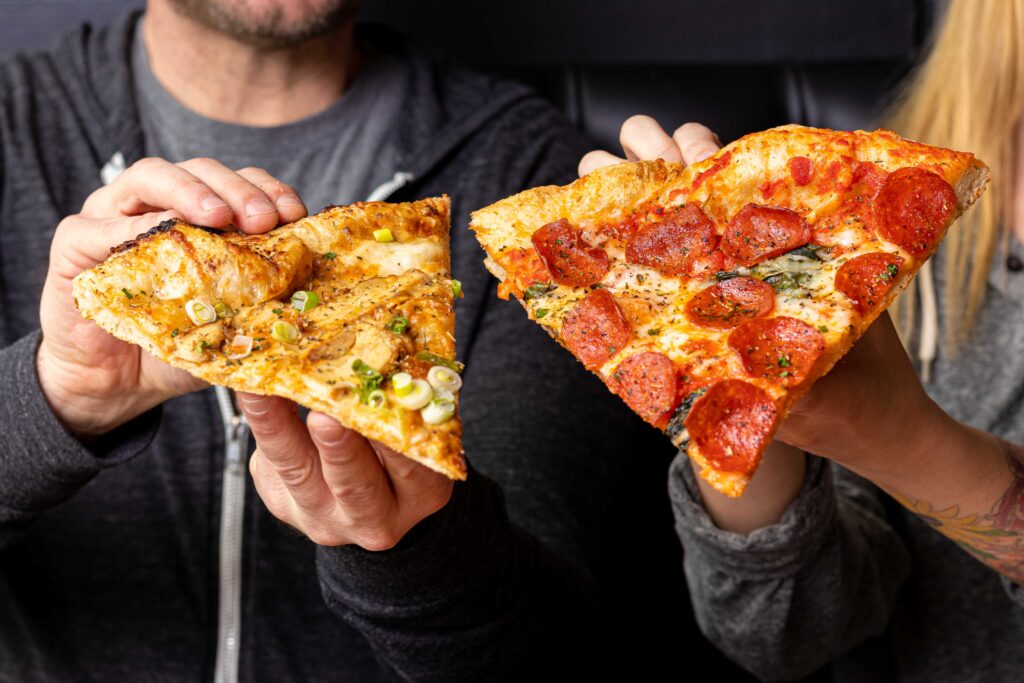 two people holding a slice of pizza up, side by side